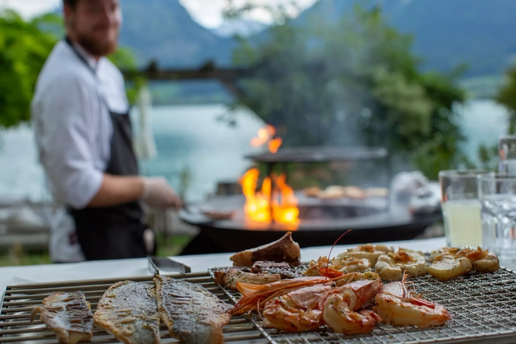 Grilled fish and shrimp on the BBQ, with a chef at Lake Wolfgang in the background.